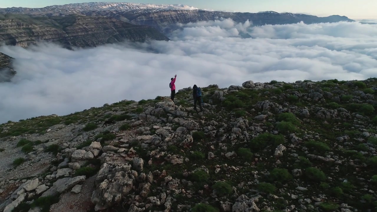 Ripresa aerea con drone di escursionisti uomini con cani sulla cima di una montagna ad Akoura, Libano