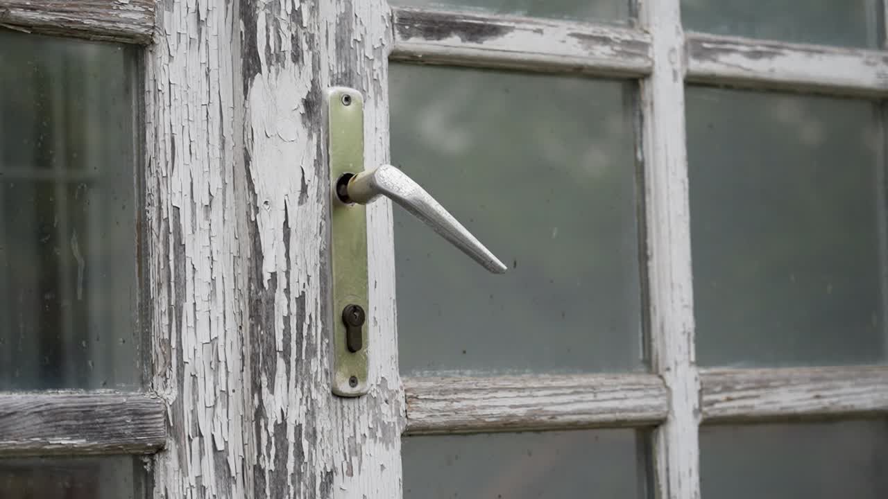 A close-up of a peeling paint door and an old metallic handle