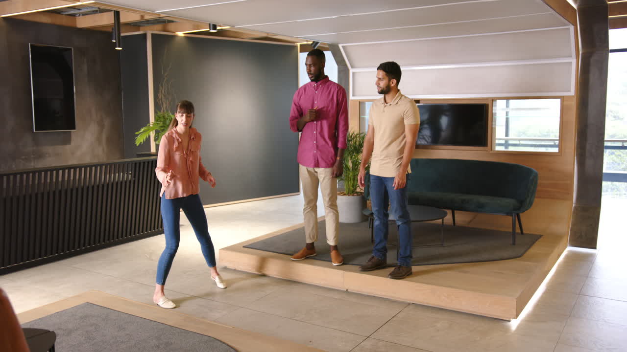 Presenting in modern office, woman speaking to two diverse colleagues on raised platform