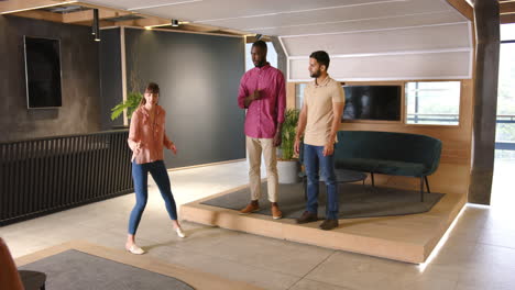 presenting in modern office, woman speaking to two diverse colleagues on raised platform
