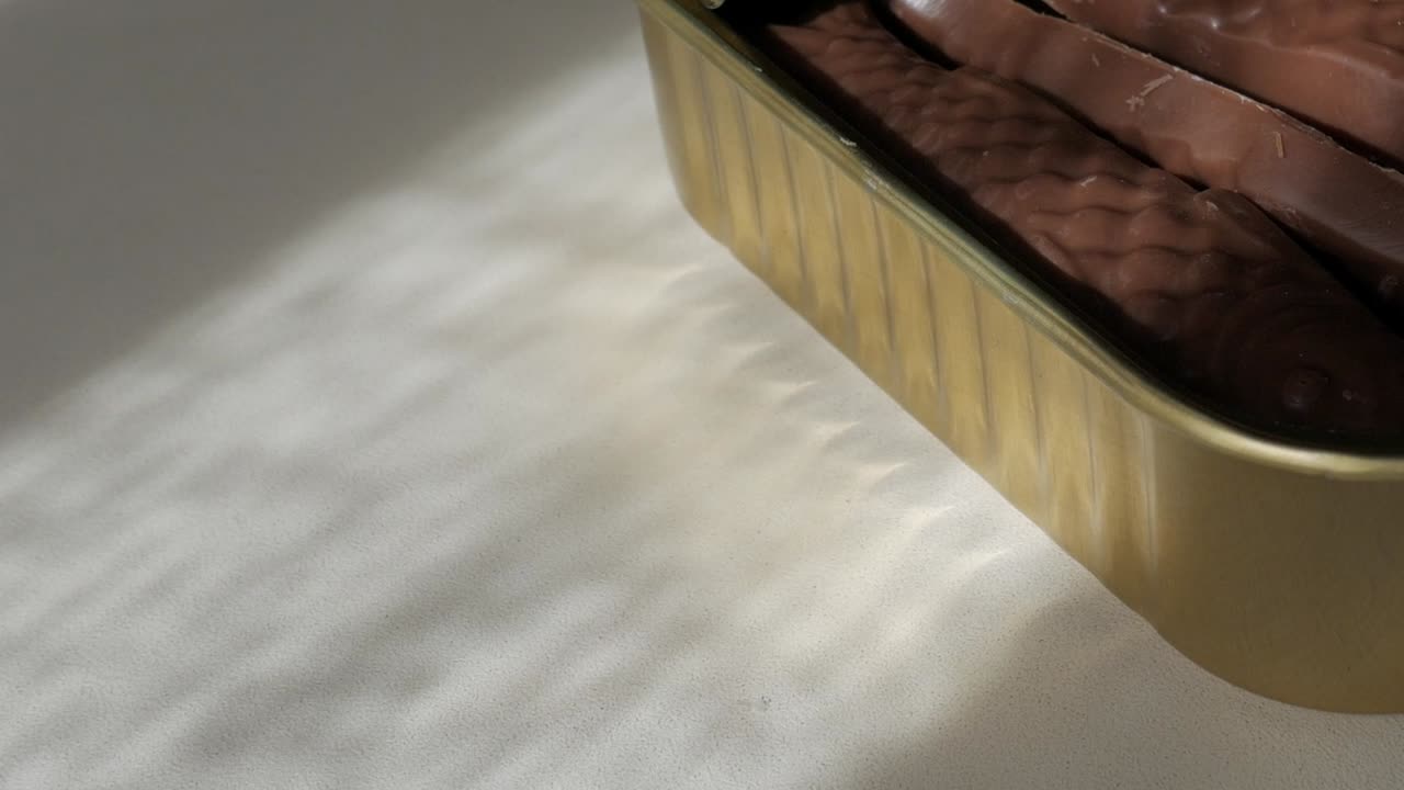 Chocolate sardines in a tin reflecting cozy sunlight shadows