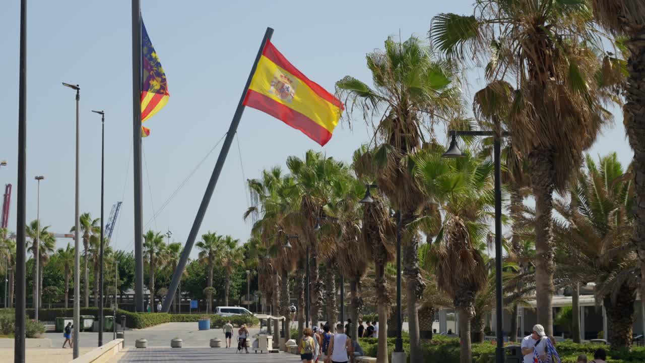Grand drapeau national espagnol flottant au vent par une chaude journée d'été près de la plage, promenade avec palmiers à Valence, Espagne