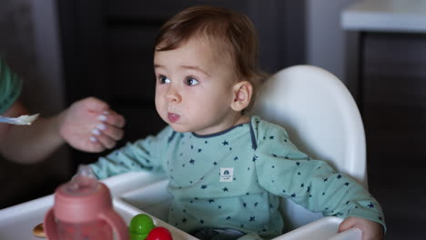 loving caring mom nourishing her little son. mother is shoving the full spoon to a calm peaceful bay boy sitting in the chair. blurred backdrop.