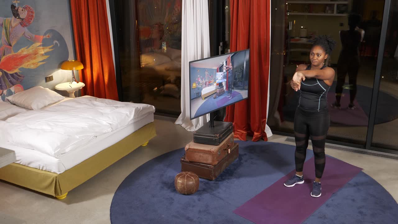 가정 환경, 밝은 방, 낮, 활동적인 생활 방식, 스트레칭에서 tv에서 운동 루틴을 따르는 여성