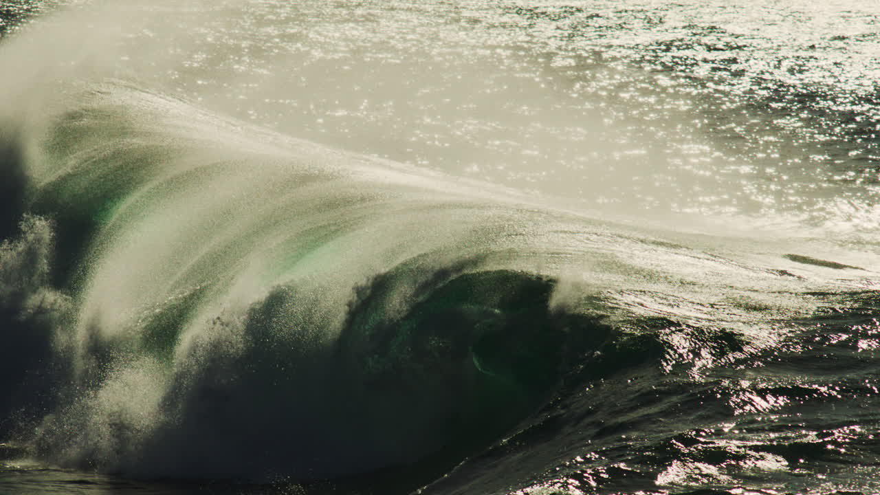 Wave collapses in sunlight as golden mist erupts off crest in cinematic slow motion crash