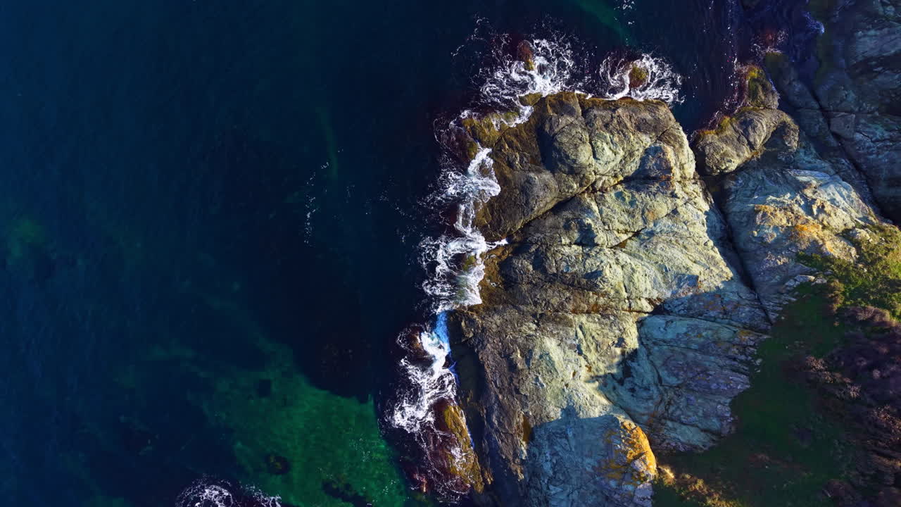 Onde calme lambiscono dolcemente la costa rocciosa sotto il sole splendente, creando una serena scena costiera a mezzogiorno.