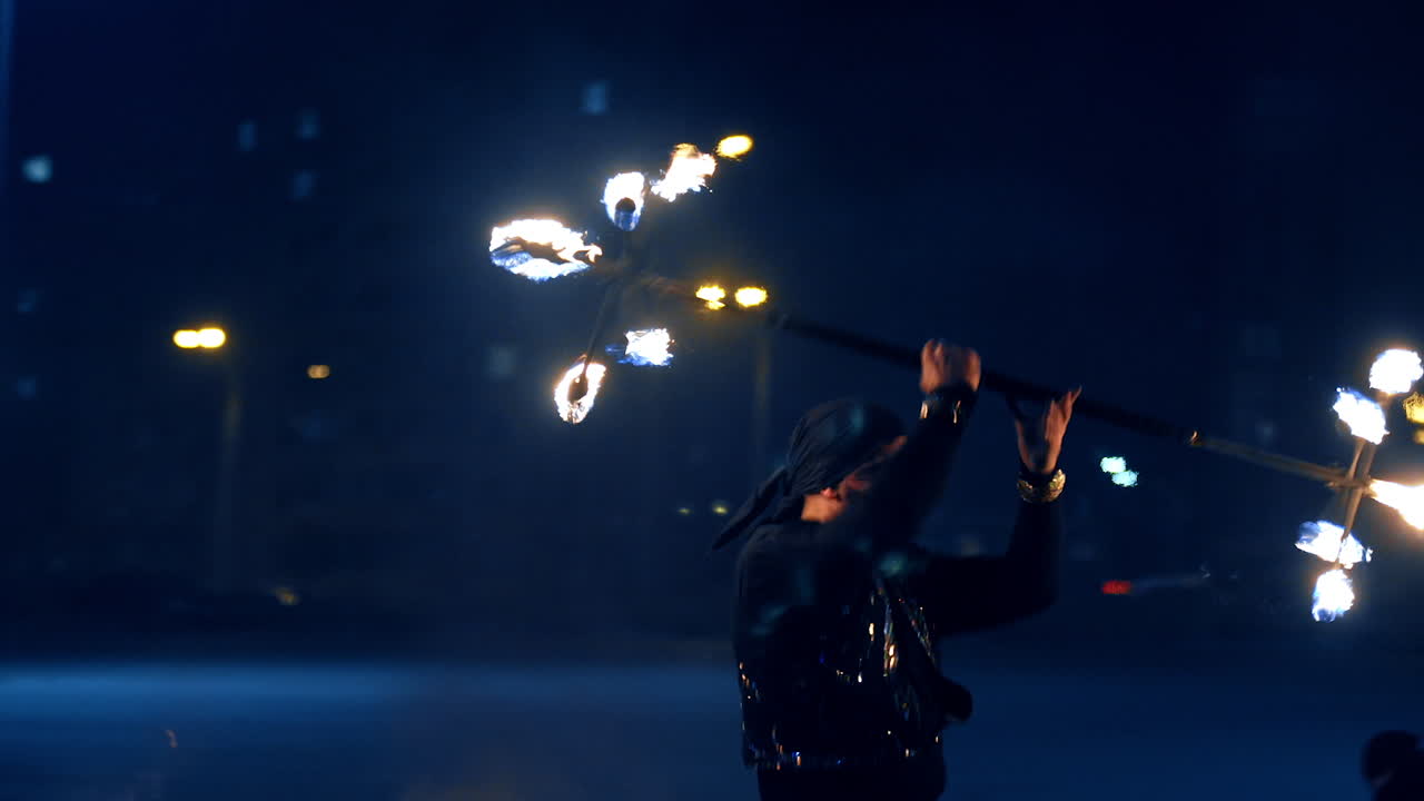 Male performer turning the burning stick over his head. Fire spectacle outdoors at night.