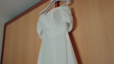 simple white wedding dress hanging on a wooden wardrobe in soft natural light