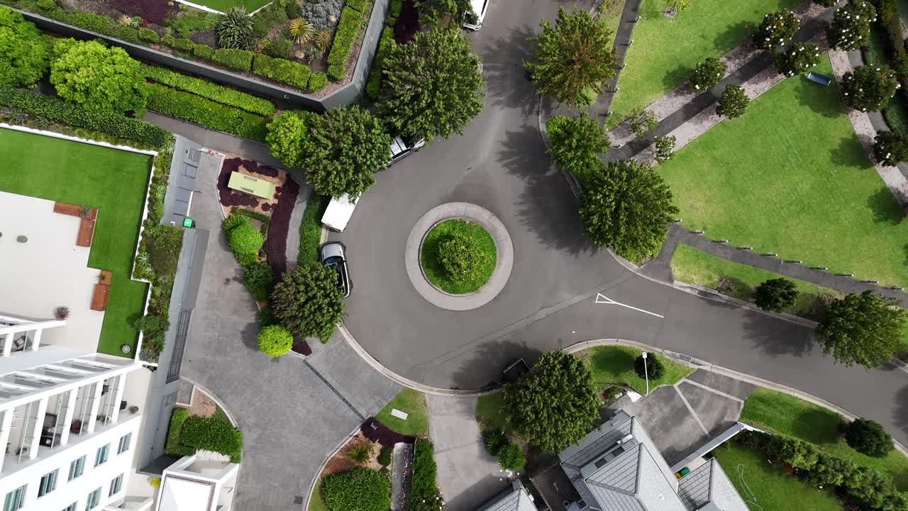 Close aerial orbit ascend of roundabout with residential apartment buildings and lush tropical greenery