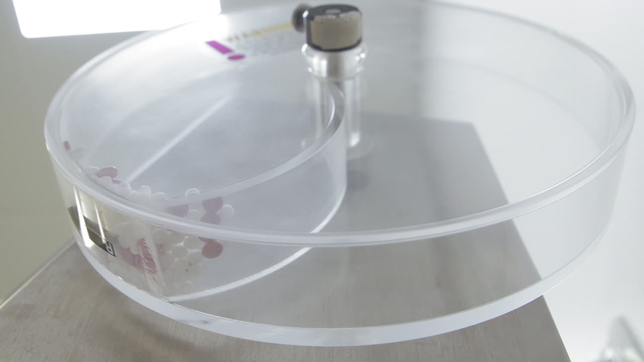 probador de friabilidad de tabletas mientras prueba píldoras rosadas y blancas en un laboratorio de investigación - toma hacia arriba