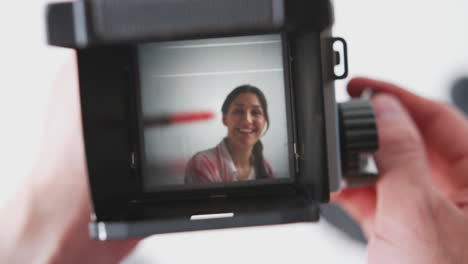 photographer looking into viewfinder of vintage medium format camera taking portrait of young woman