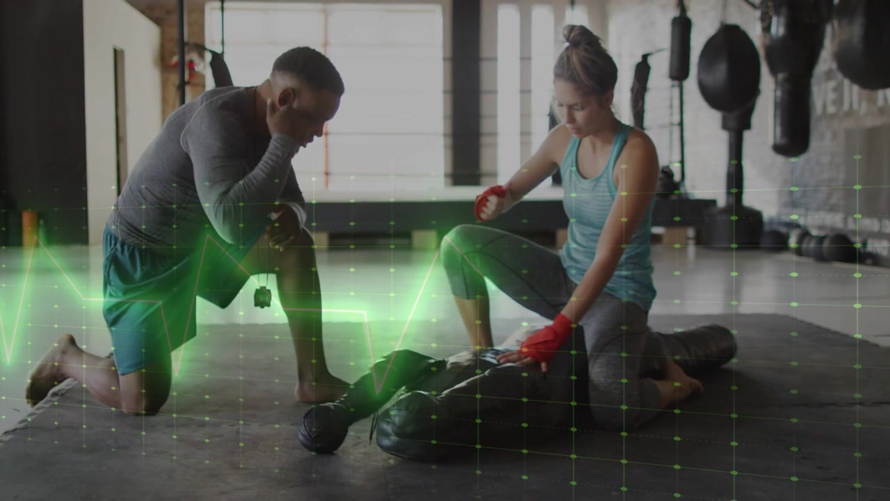 Entrenador gesticulando, aprendiz revisando guantes rojos en saco, cuadrícula verde mostrando forma, preparándose para golpear en gimnasio.