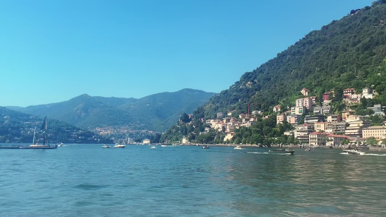 Barche che passano in una splendida giornata estiva sul Lago di Como. Il bellissimo lago è circondato da case italiane e alte montagne.