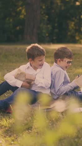 cute happy diligent kids in shirts prepare for school test with books sitting on lush grass in green school garden