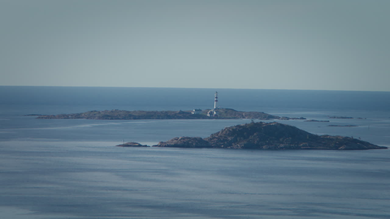 Static wide shot zooming in on a lighthouse situated on a small rocky island in Kristiansand Norway on a clear sunny day