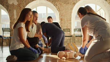 Close-up-shooting:-A-professional-nurse-girl-in-a-white-medical-uniform-conducts-medical-training-in-first-aid-with-a-baby-dummy.-Black-man-in-blue-medical-uniform-performs