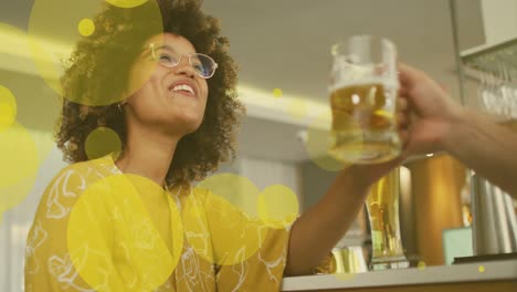 Animation-of-spots-over-happy-biracial-woman-with-caucasian-friend-drinking-beer