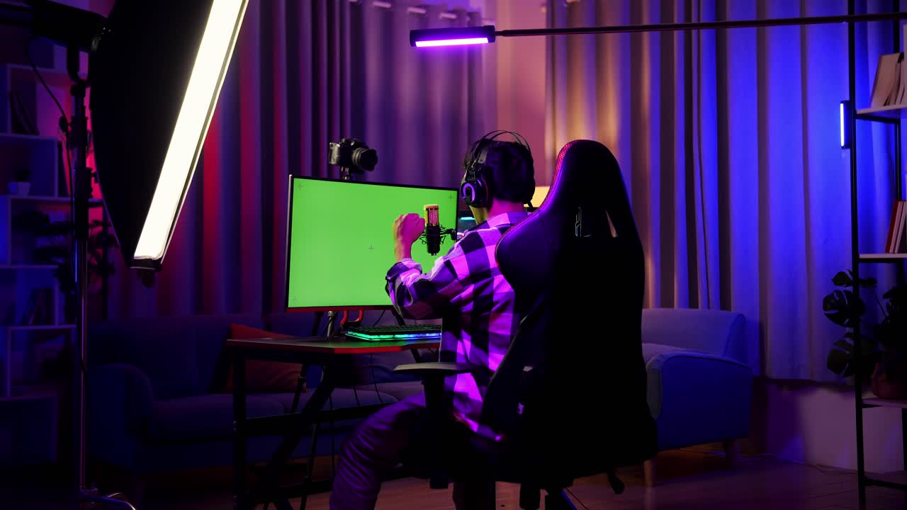Vista Posteriore Di Un Ragazzo Streamer Asiatico Che Urla "Gol" Celebrando La Vittoria Di Una Partita Su Computer Con Schermo Verde. Live Stream Su Scrivania Illuminata Da Striscia LED RGB.