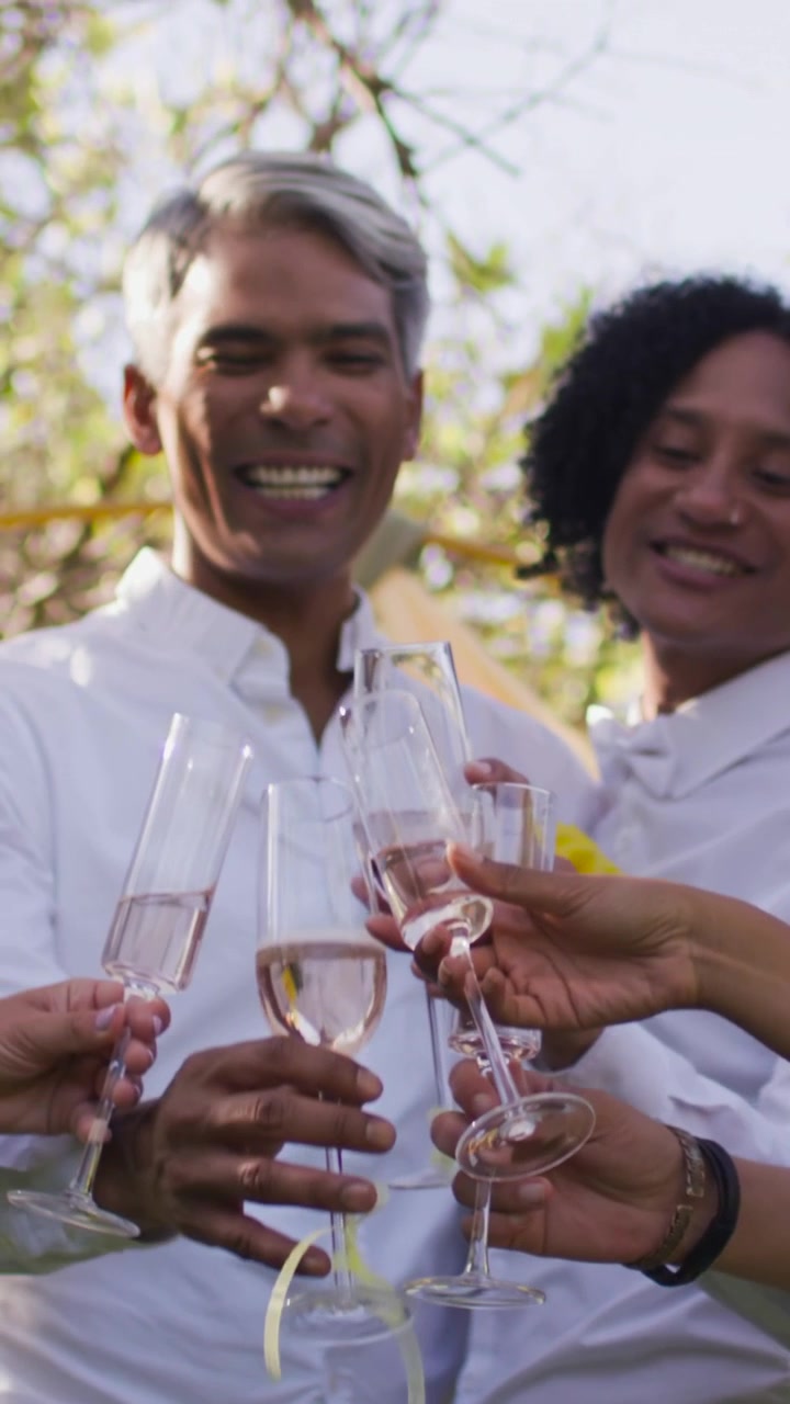 Vertical video: Raising glasses guests, woman in tan top clinking flutes in garden, marking moment