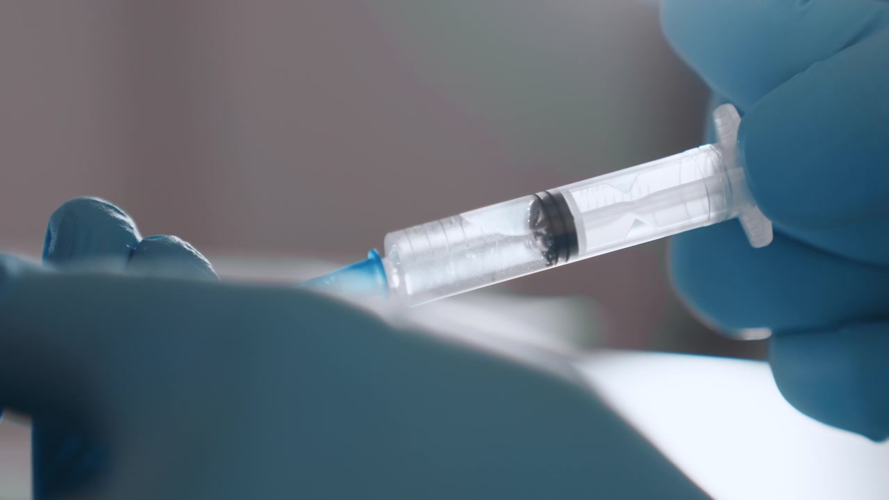 Closeup syringe injection by black nurse during home visit, gloved hands steady, patient arm exposed, warm domestic lighting, sterile technique, caring interaction, emergency kit visible