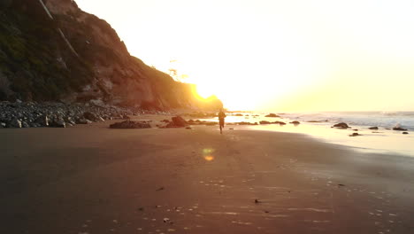 A-man-athlete-in-silhouette-running-fast-on-a-beach-at-sunrise-during-a-fitness-cardio-workout-in-Santa-Barbara,-California-AERIAL-DRONE