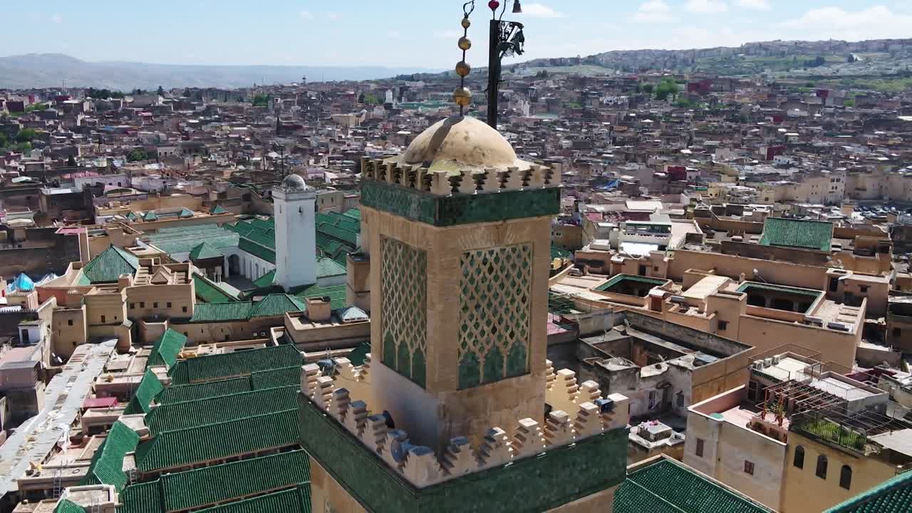 Detailed drone close-up of the historic Al-Qarawiyyin mosque minaret. Features the intricate green Zellige mosaic, copper jamour, and a panoramic backdrop of the world's oldest university