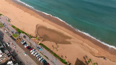 aerial dolly in of recaña sand beach and turquoise sea near hillside with luxury apartments, chile
