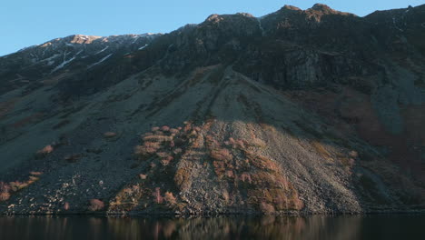 mountainside approach along lake surface with sunset rays grazing rock at wastwater lake district uk