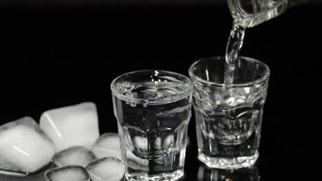 Pour-vodka-into-shot-glasses-with-ice-cubes-placed-on-a-black-background