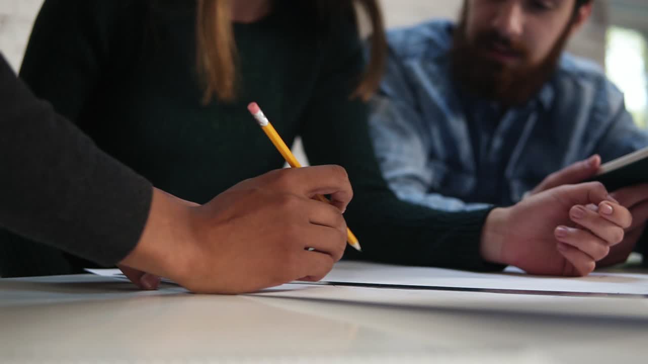 trabajador de oficina africano sonriente dibujando un proyecto de pie junto a la mesa mientras sus colegas lo ayudan. grupo multiétnico de