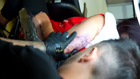 artist tattooing client's dog's name under dog's face design on her arm. vertical shot