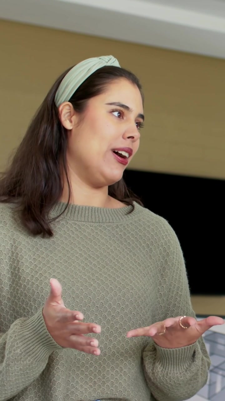 Vertical video: Opening with palm out, woman explaining, gesturing at home, olive sweater and rings