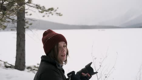 a young female photographer smiles and uses camera in snowy forest, fixed medium