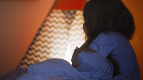 una niña enferma con un edredón caliente frota la cara en la cama cerca de la tienda