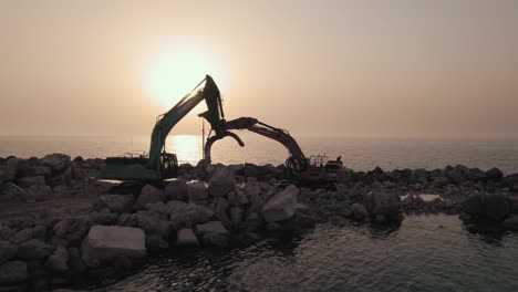 sunset silhouette of two excavators standing on a breakwater they constructed