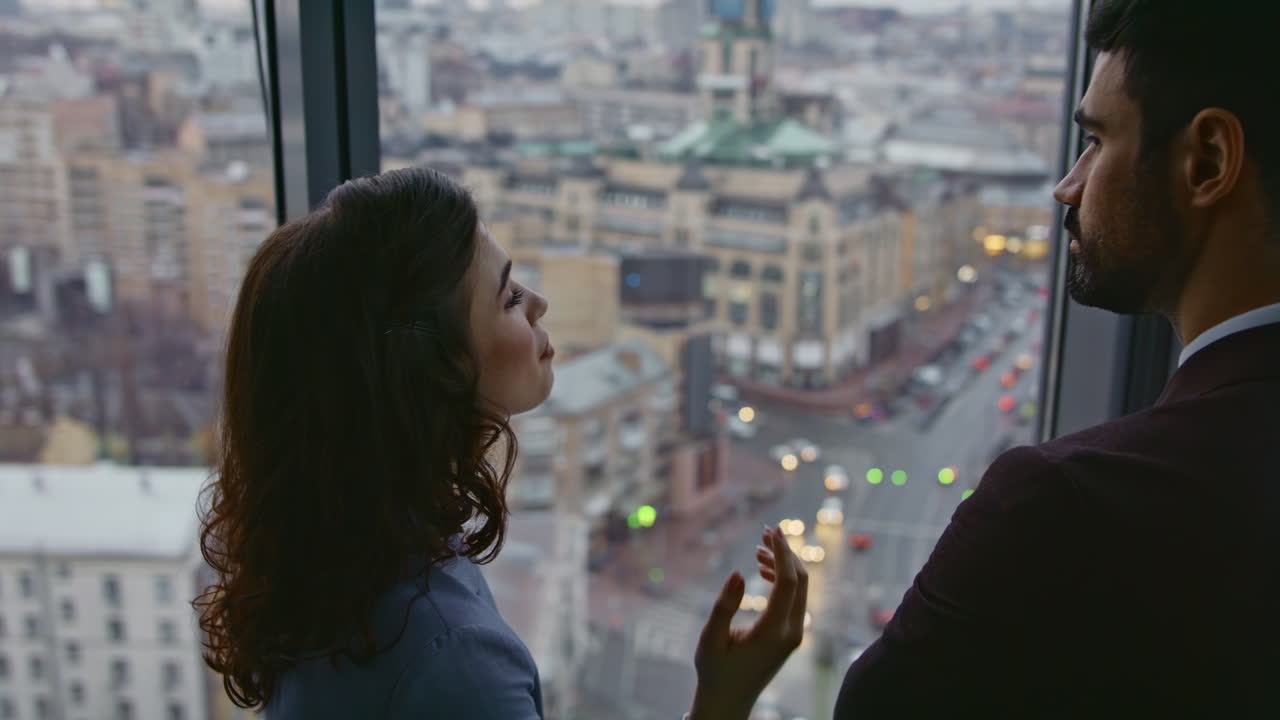 pareja de colegas que se comunican de pie en la oficina mirando la ventana del paisaje urbano en primer plano