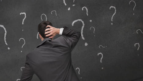 rear view of confused caucasian businessman scratching head, with question marks on chalkboard