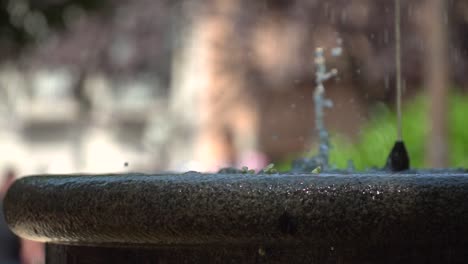 Nahaufnahme-Des-Wasserbrunnens,-Der-Wasser-Mit-Verschwommenem-Bokeh-Hintergrund-In-Zeitlupe-Im-Park-Ausspuckt