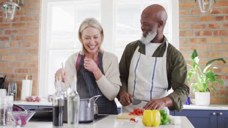mixed race senior couple having fun while cooking food together in the kitchen at home