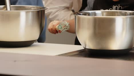 hands mixing with a whisk in stainless steel bowls on a kitchen counter