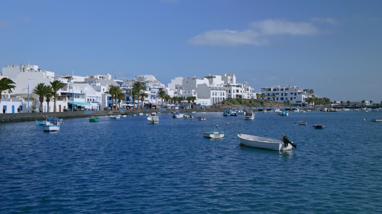 Il villaggio costiero di Arrecife a Lanzarote, Isole Canarie, con edifici bianchi, palme e barche sull'acqua blu. Una pittoresca destinazione di viaggio sotto un cielo sereno.