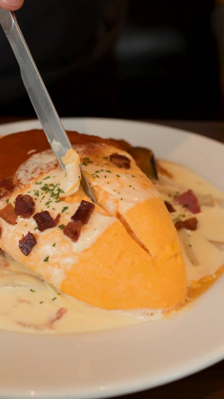 Un coltello taglia soffice riso omelette, salsa cremosa e condimenti, in un ambiente di ristorante illuminato calorosamente.