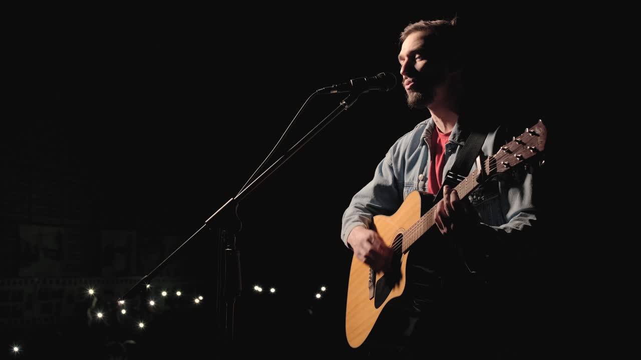 A musician is playing guitar on a large stage with audience members holding flashlights in the background. The auditorium is filled with beautiful flashing lights.