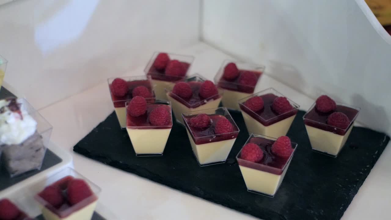 Close-up handheld shot of elegant custard cups topped with raspberry sauce.