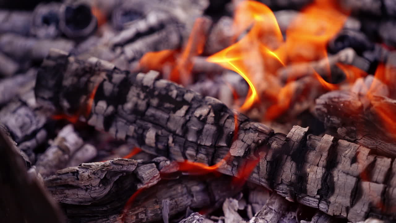 Coals are burning in the fire. Smoldered logs with slight flame background. Fire transforms the wood into charcoal. Close-up. Slow motion