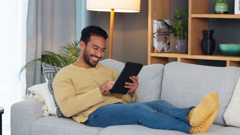 Young-man-happily-laying-on-couch-with-tablet