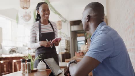 Happy-african-american-female-barista-taking-order-from-male-customer-using-tablet,-slow-motion