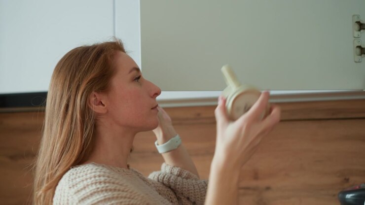 Woman in cozy knit sweater reaches for and holds ceramic mug with soft natural light illuminating scene. background features wooden cabinetry and white upper cabinets creating warm home