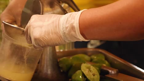a person uses a metal juicer to extract lime juice, wearing gloves for hygiene.
