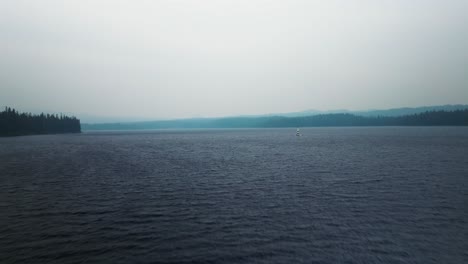 Aerial-dolly-over-foggy-cold-lake-to-sunfish-sailboat-on-windswept-water